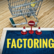 shopping cart with a blackboard, yellow letters say "factoring" with safety cones and sign