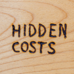 The words "hidden costs" burned into wood