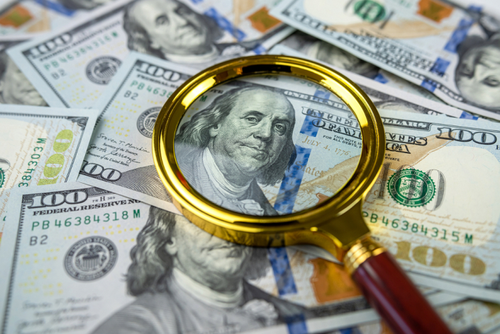 magnifying glass looking at $100 bill for fake money